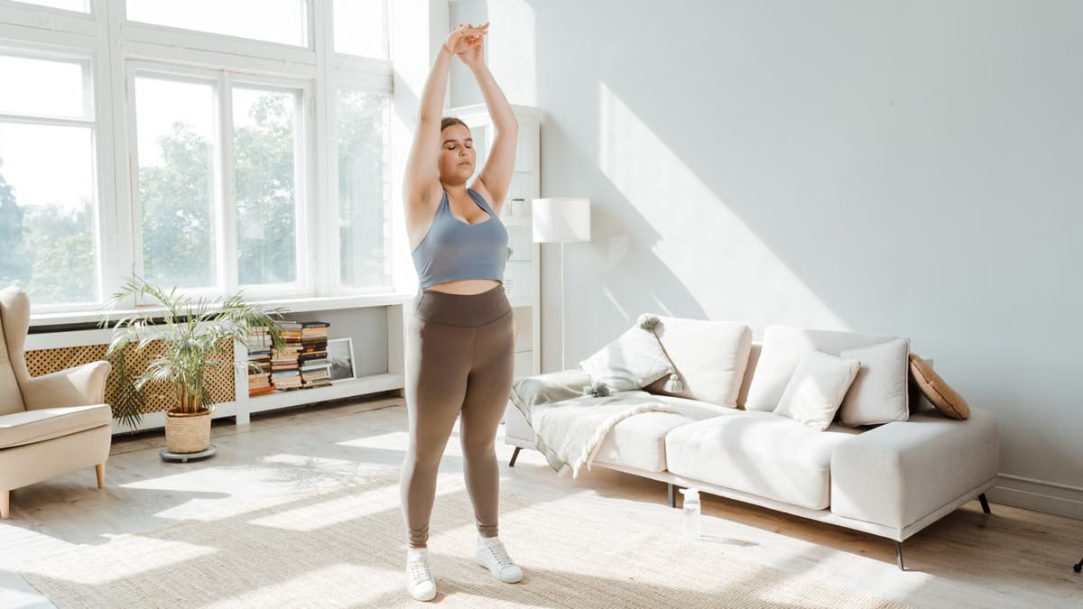 Woman in activewear stretching in a bright living room, embracing a healthy lifestyle.